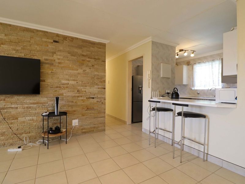 Open plan living area featuring a stone accent wall, tiled flooring, and a functional kitchen with a breakfast bar counter.