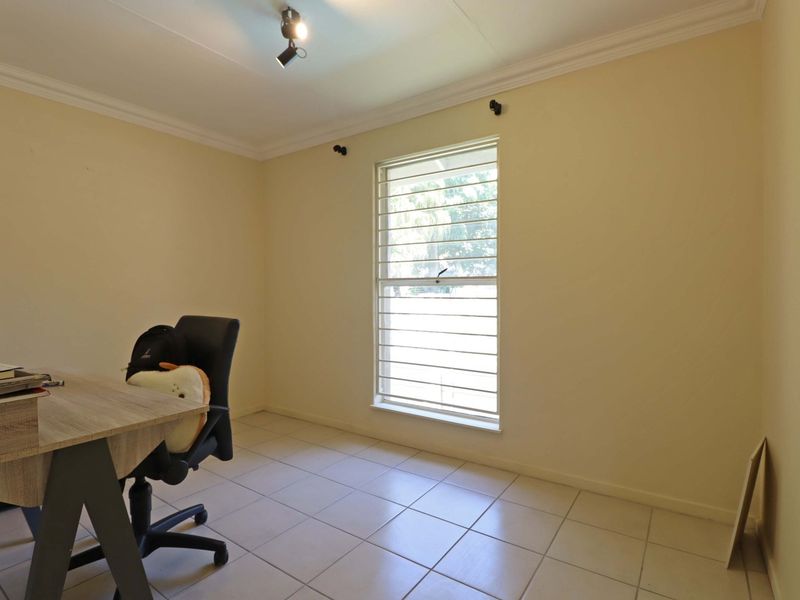 A functional bedroom featuring tiled flooring, security bars on the window, and ceiling-mounted spotlighting.