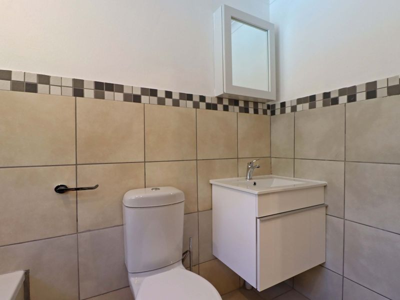 A clean and functional bathroom featuring a modern wall-mounted vanity, basin, and toilet with neutral wall tiling and a decorative border.