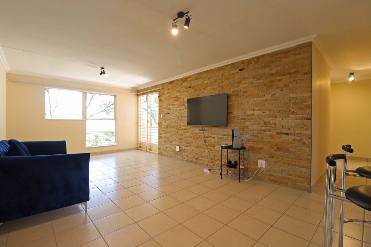 Spacious living area featuring a textured stone accent wall, neutral tiled flooring, and ample natural light through large windows.