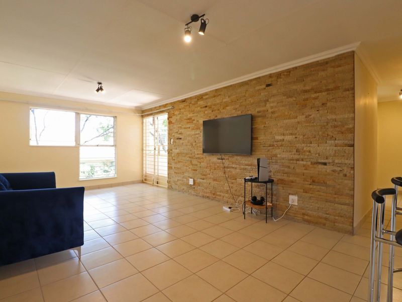 Spacious living area featuring a textured stone accent wall, neutral tiled flooring, and ample natural light through large windows.