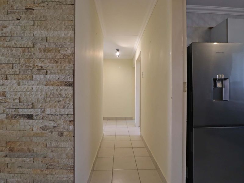 A clean, well-lit hallway featuring a decorative stone-clad feature wall and neutral tiled flooring, providing a bright transition between living spaces.