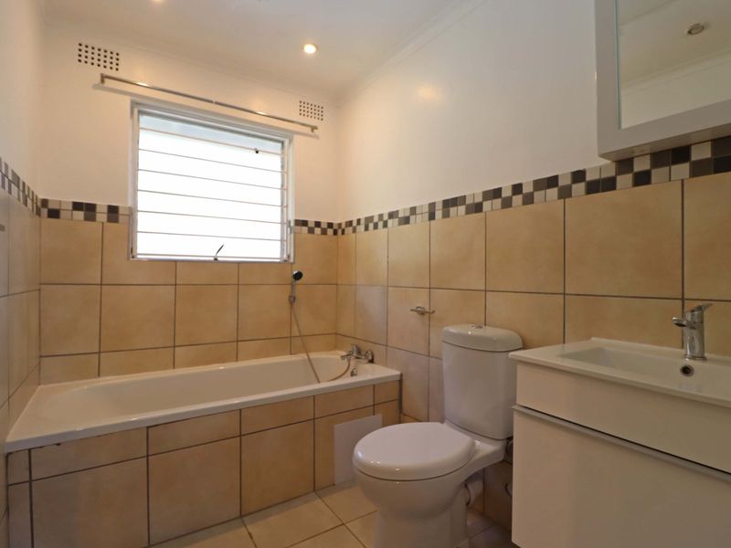 A clean, functional bathroom featuring a bathtub, toilet, and a modern vanity basin with neutral wall and floor tiling.