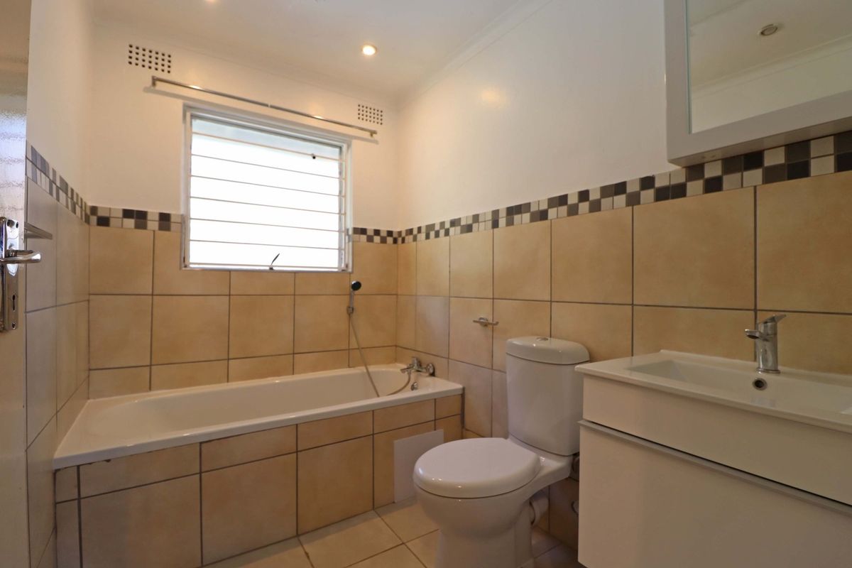 A clean, functional bathroom featuring a bathtub, toilet, and a modern vanity basin with neutral wall and floor tiling.