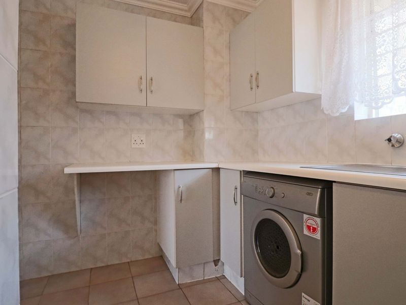 A functional laundry area featuring tiled walls and flooring, built-in cabinetry, a stainless steel sink, and dedicated space for a washing machine.