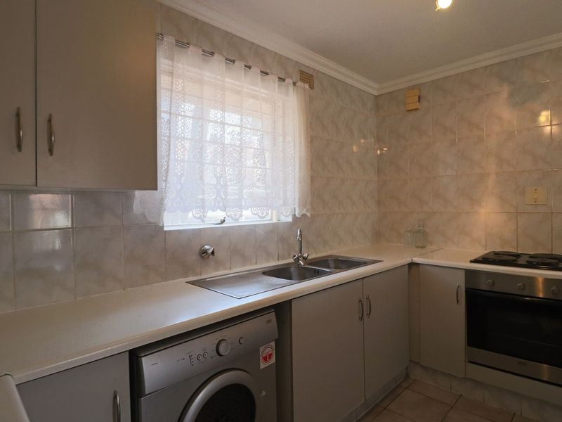 A functional kitchen featuring built-in cabinetry, a double sink, tiled splashbacks, and integrated oven and hob appliances.
