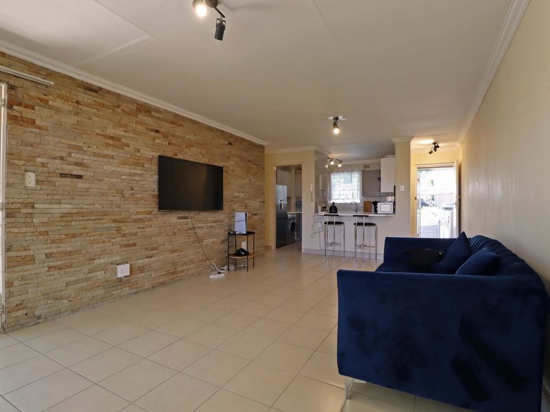 Open-plan living area featuring a prominent stone accent wall, tiled flooring, and an integrated kitchen with a breakfast counter.