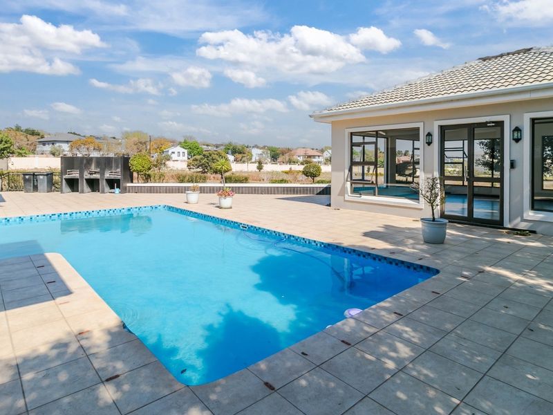 Spacious outdoor pool area featuring a large swimming pool, tiled patio, and a built-in braai, perfect for outdoor entertaining.
