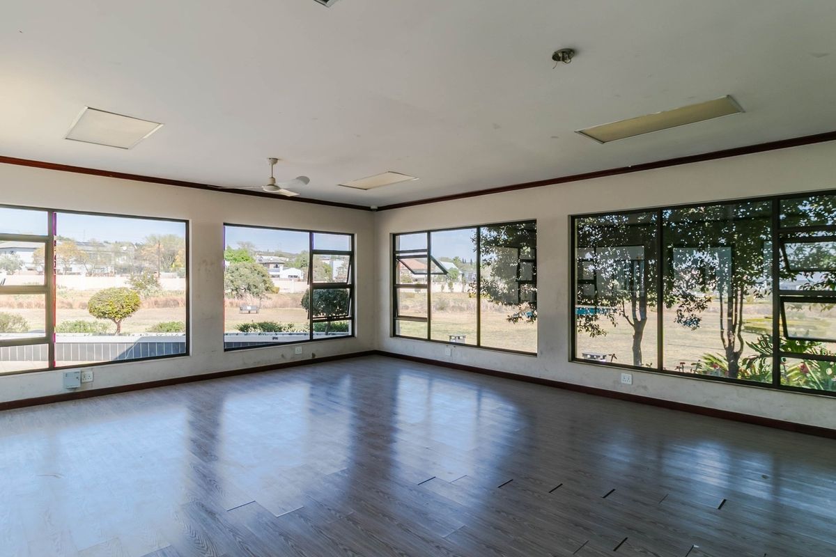 Spacious, empty living area featuring extensive aluminium-framed windows providing natural light and garden views, finished with laminate flooring and ceiling fan.