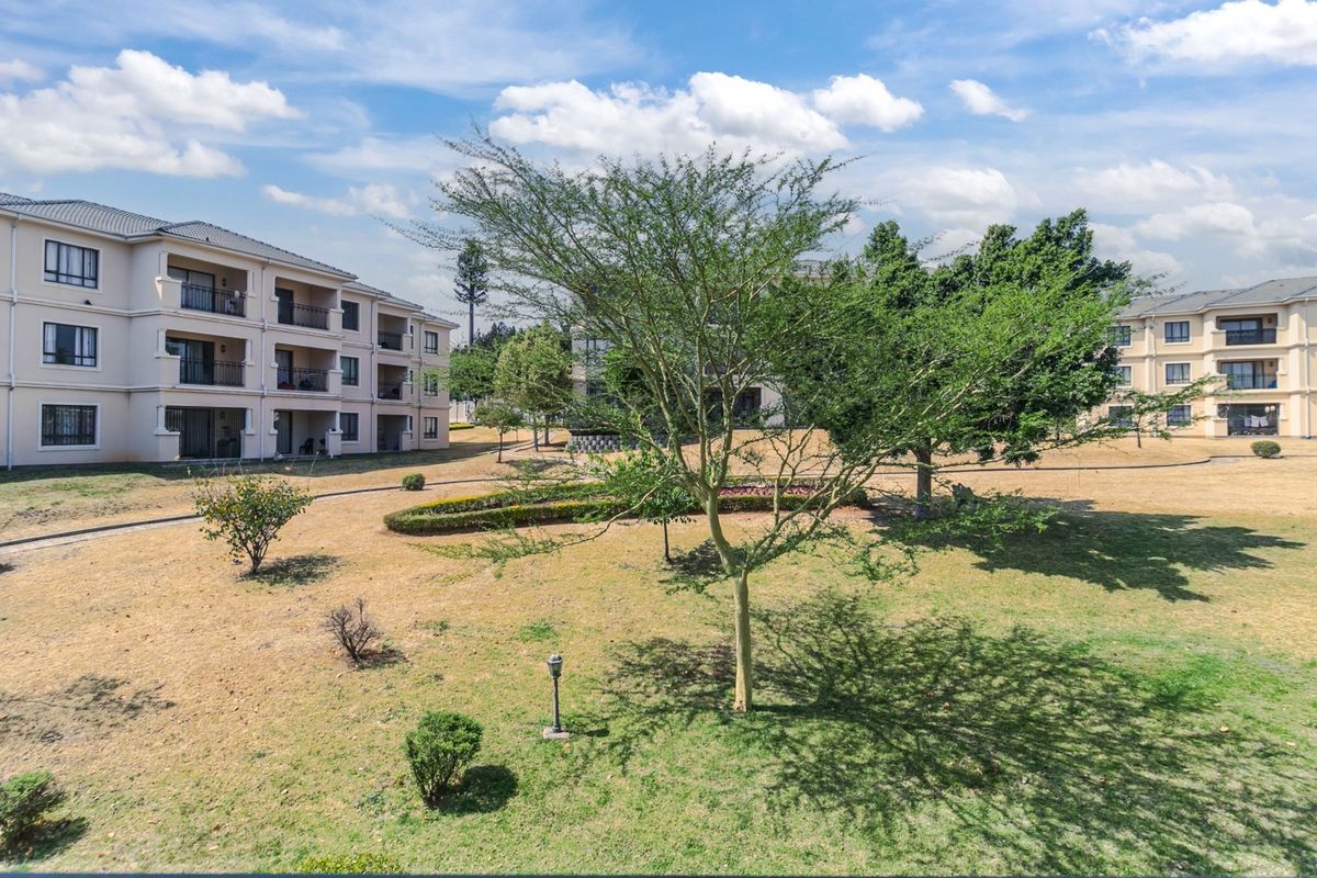 A view of the apartment complex exterior featuring landscaped communal gardens, paved pathways, and multi-story residential buildings with private balconies.