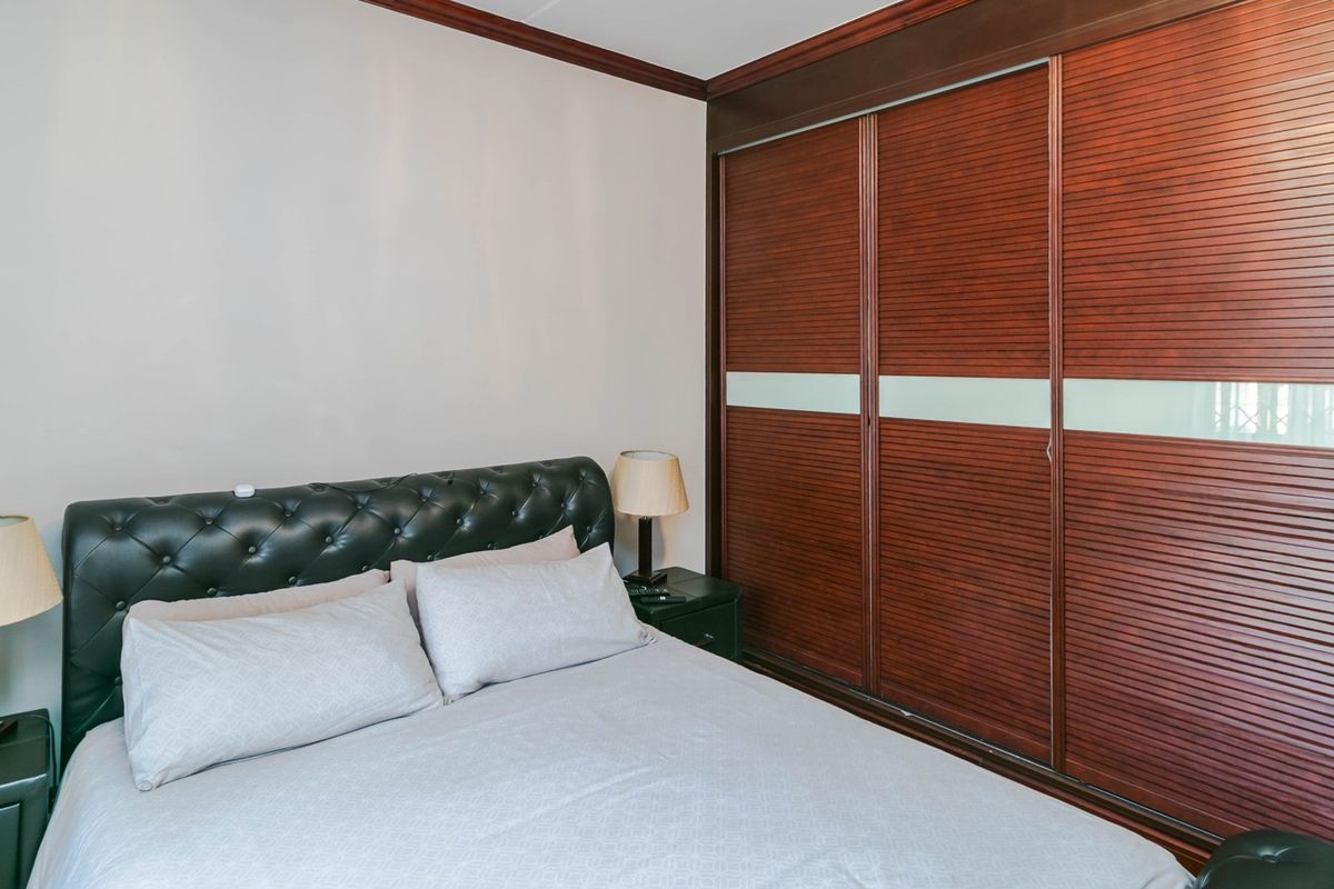 A well-maintained bedroom featuring a large, dark wood built-in sliding door wardrobe and classic crown molding details.