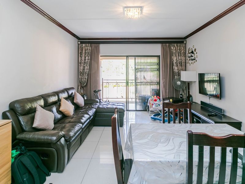 Open-plan living and dining area featuring tiled flooring, crown molding, and a sliding glass door leading to a balcony with security gate.