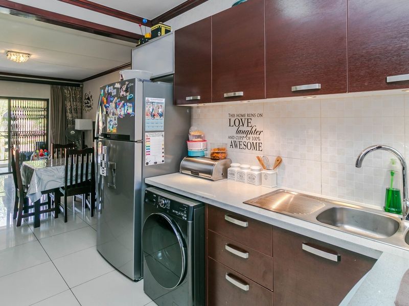 Open-plan kitchen featuring dark wood cabinetry, tiled backsplash, and integrated sink, flowing into a dining and living area with balcony access.