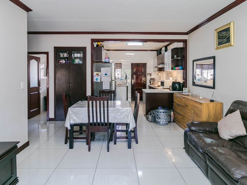 Open-plan living and dining area featuring tiled flooring, crown molding, and a connected kitchen space with built-in cabinetry.