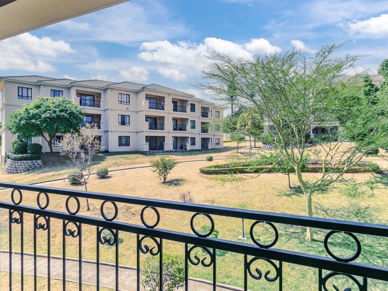 A view from a balcony overlooking a well-maintained communal garden and adjacent apartment building complex.