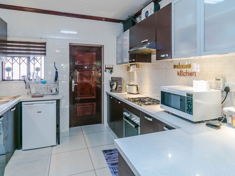A well-maintained kitchen featuring dark wood cabinetry, stone countertops, a gas hob, built-in oven, and tiled finishes throughout.