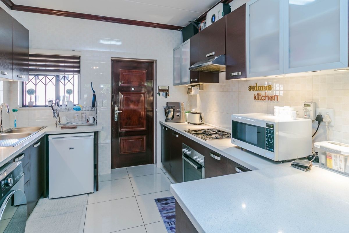 A well-maintained kitchen featuring dark wood cabinetry, stone countertops, a gas hob, built-in oven, and tiled finishes throughout.