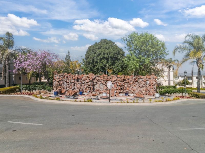 A view of the apartment complex entrance featuring a landscaped roundabout with a decorative stone feature wall and mature trees.