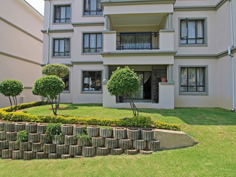 Rear view of the apartment building featuring a landscaped garden with a concrete retaining wall, private balconies, and large windows.