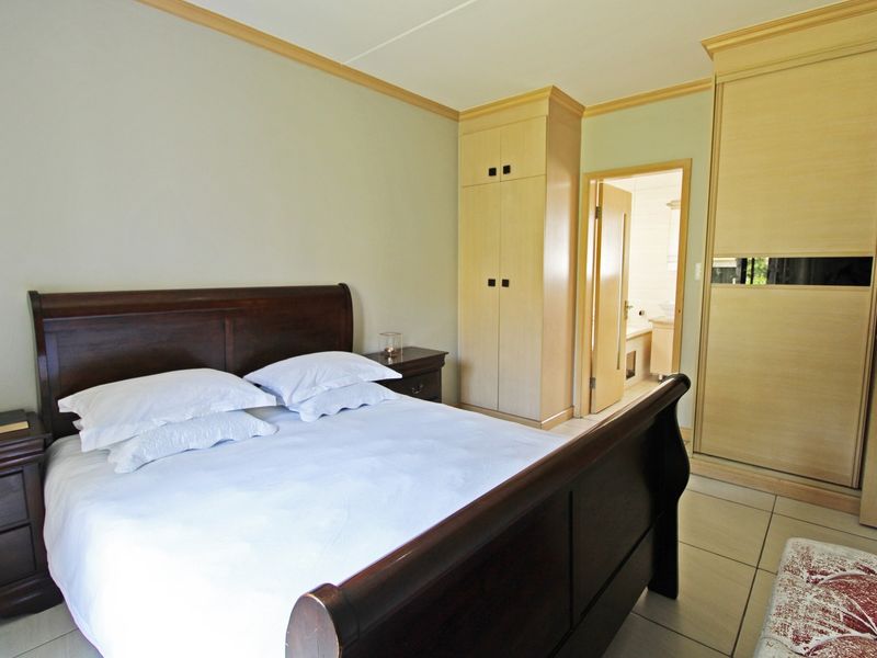 A bedroom featuring built-in wooden cupboards, tiled flooring, and direct access to an en-suite bathroom.