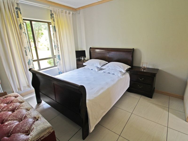 A functional bedroom featuring tiled flooring, a built-in wardrobe, and natural light through an aluminium-framed window.