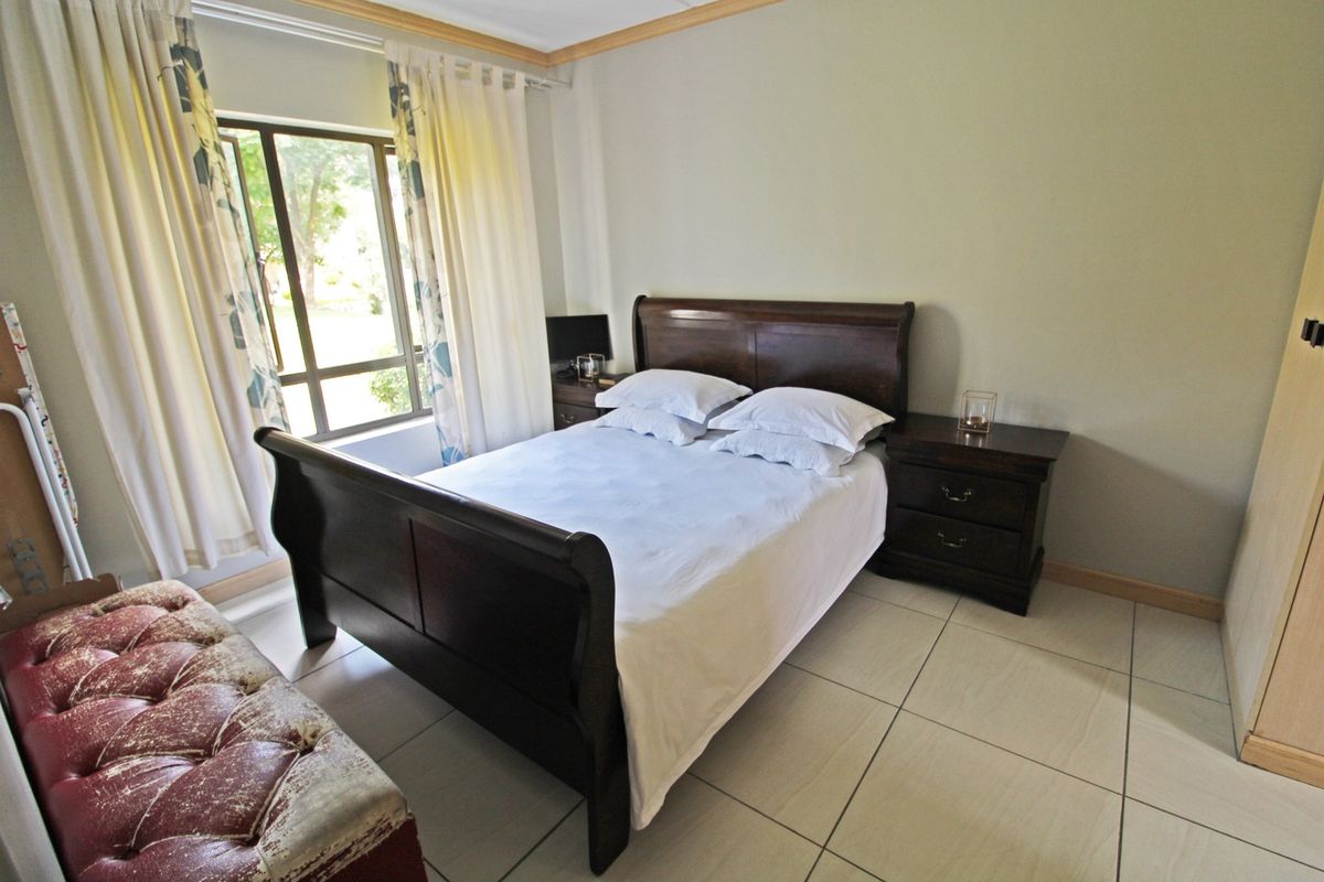 A functional bedroom featuring tiled flooring, a built-in wardrobe, and natural light through an aluminium-framed window.