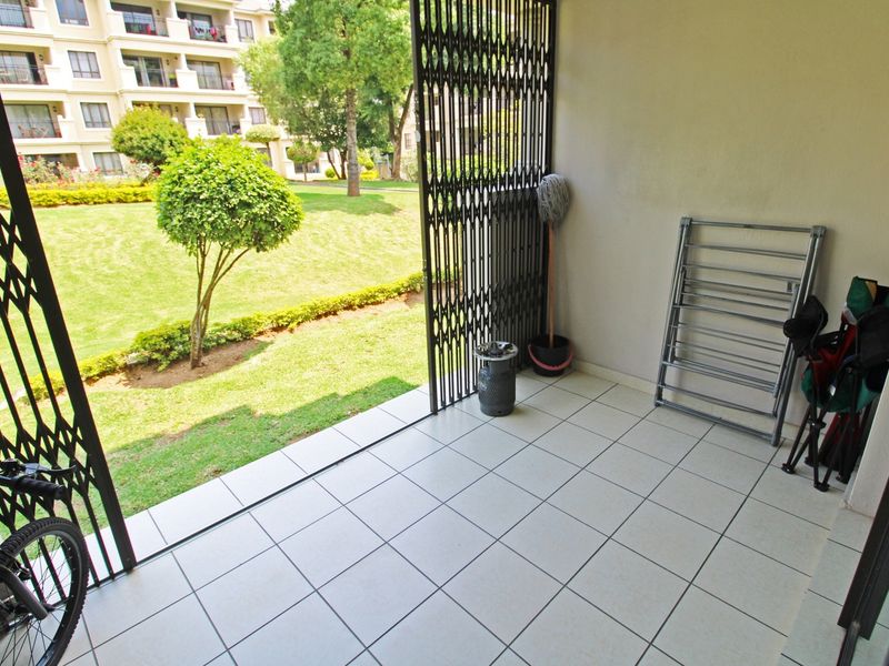 A covered patio area featuring tiled flooring and a security gate, providing direct access to the communal garden space.