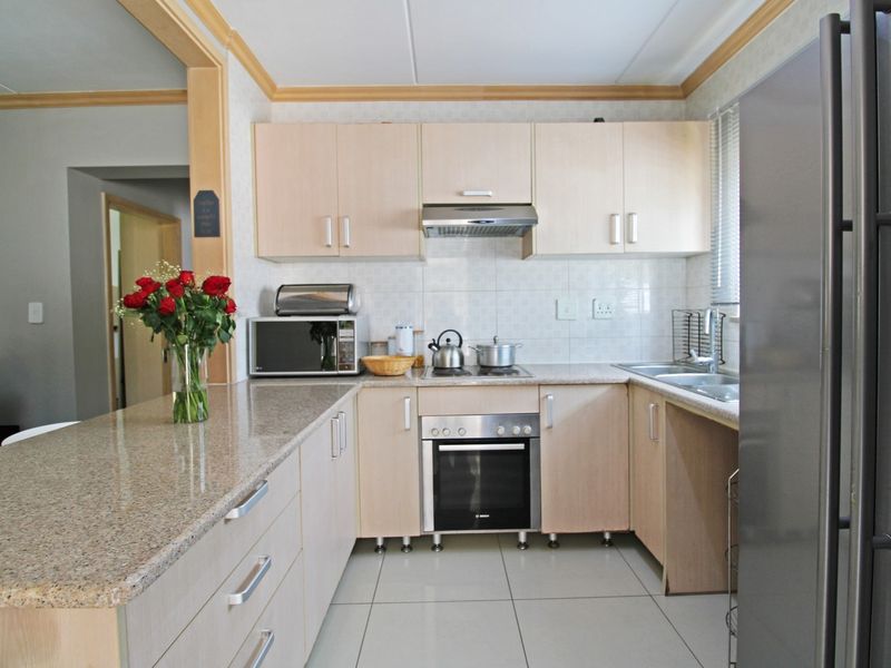 A functional kitchen featuring granite countertops, light wood-finish cabinetry, built-in oven, hob, extractor fan, and tiled flooring.