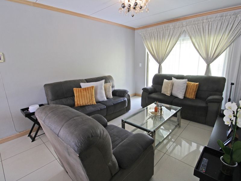 A comfortable living room featuring neutral tiled flooring, ceiling cornicing, and a large sliding glass door providing natural light.