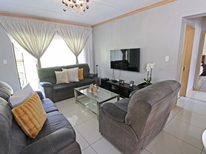 A well-maintained living room featuring neutral tiled flooring, decorative ceiling cornicing, and a sliding glass door providing natural light.
