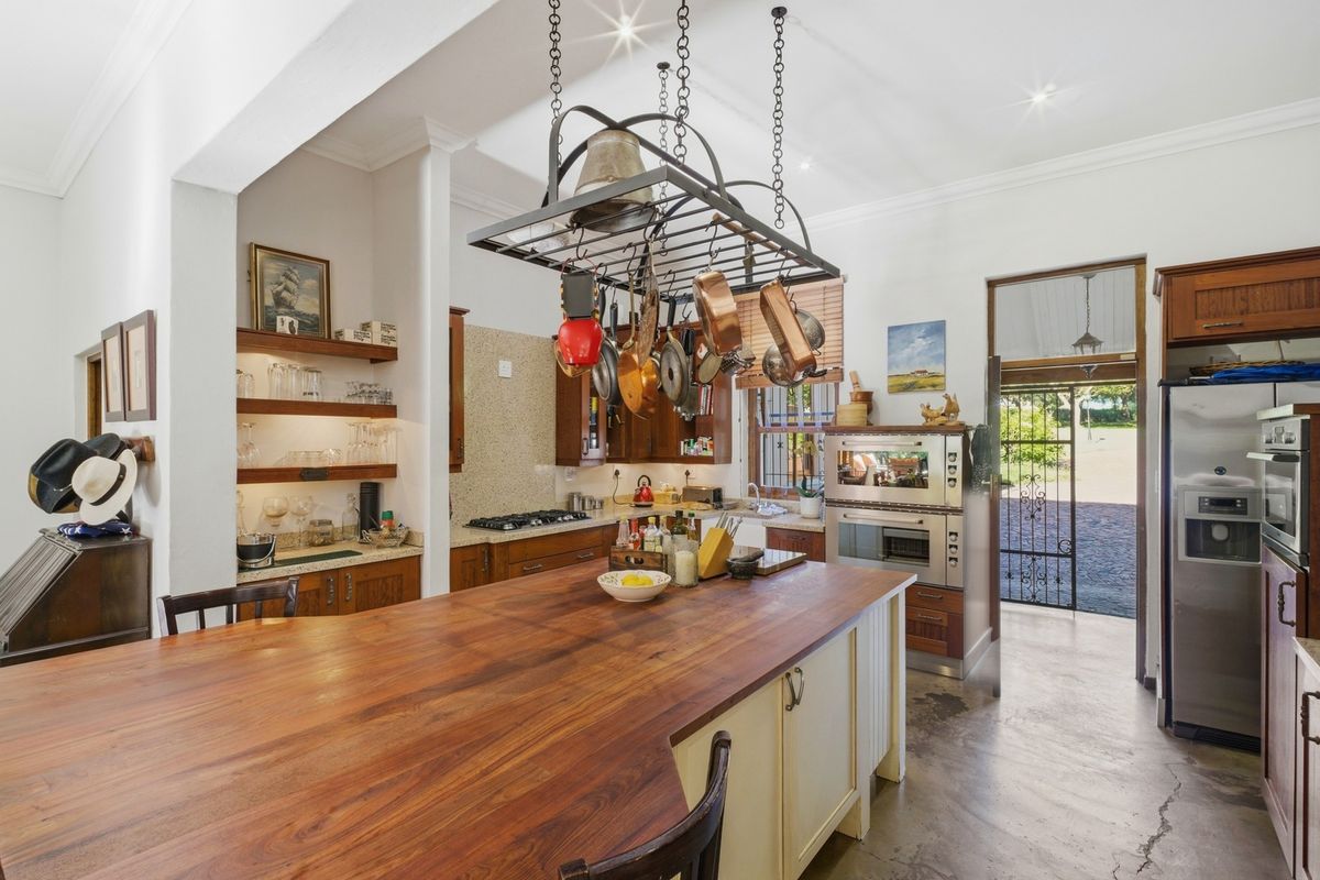 A spacious kitchen featuring a large wooden island, built-in oven, gas hob, and custom cabinetry with a stone backsplash and concrete flooring.
