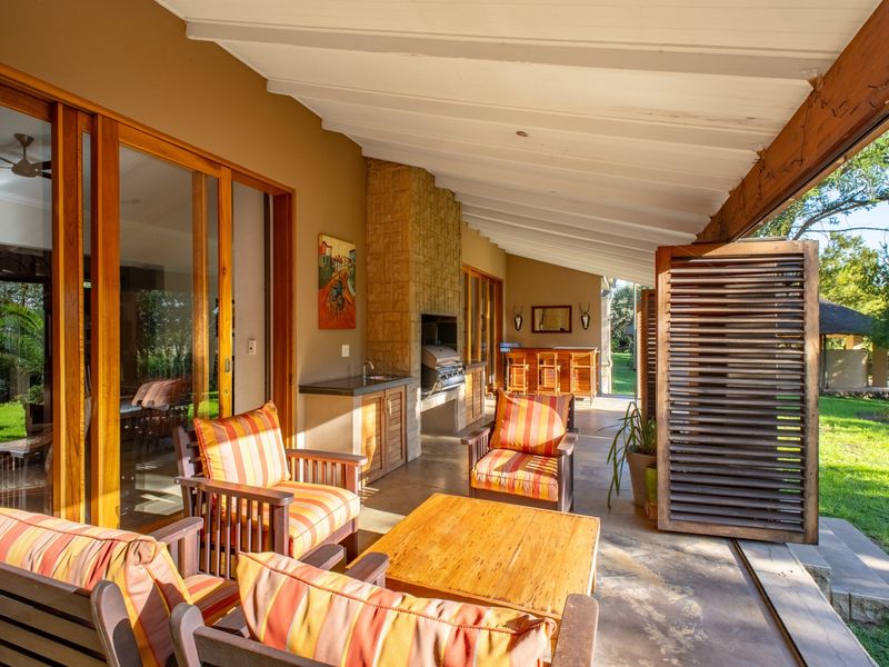 Spacious covered patio featuring a built-in braai, stone-clad fireplace, outdoor sink, and large wooden sliding doors opening to the garden.