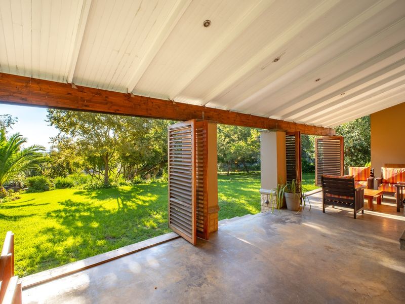A spacious covered patio featuring timber beams, recessed lighting, and stone-clad pillars, opening directly onto a lush green garden.