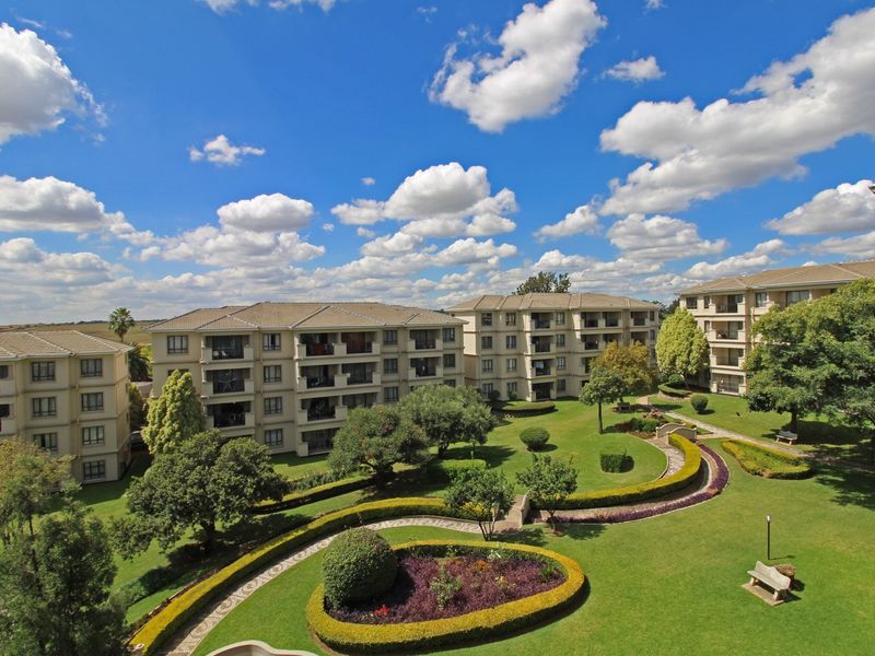 Elevated view overlooking a well-maintained apartment complex with landscaped gardens, manicured hedges, and paved pathways between residential buildings.