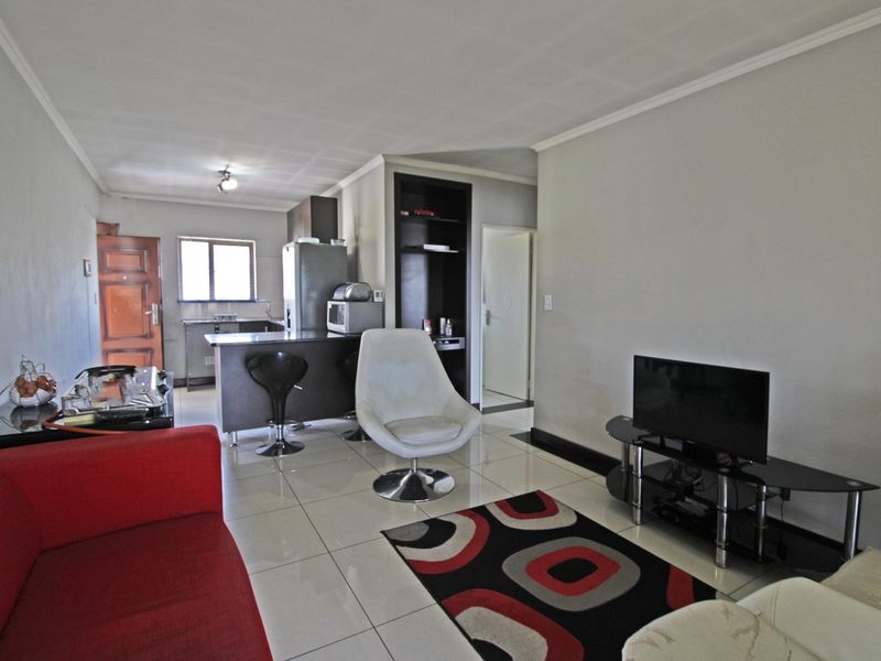 Open-plan living area featuring tiled flooring, a compact kitchen with a breakfast bar, and built-in shelving, creating a functional and connected living space.