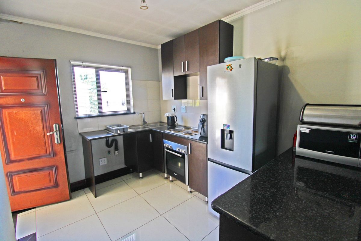Compact kitchen featuring dark wood cabinetry, granite countertops, built-in oven, electric hob, and tiled flooring with direct access to an exterior door.