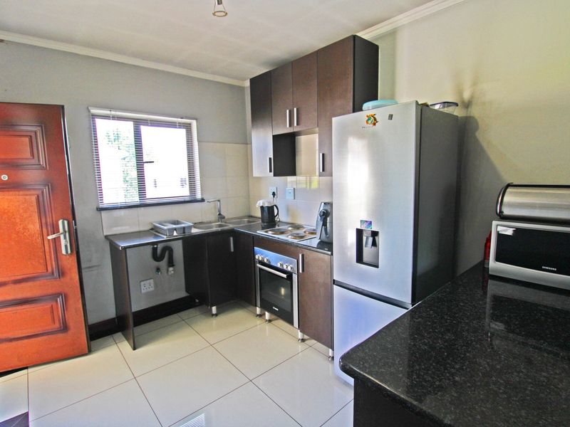 Compact kitchen featuring dark wood cabinetry, granite countertops, built-in oven, electric hob, and tiled flooring with direct access to an exterior door.
