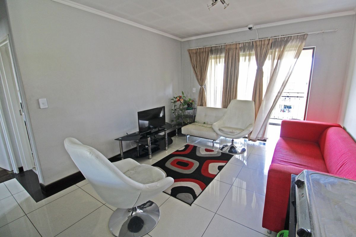 A bright living room featuring large format floor tiles, coving, and a sliding glass door providing access to an outdoor balcony area.