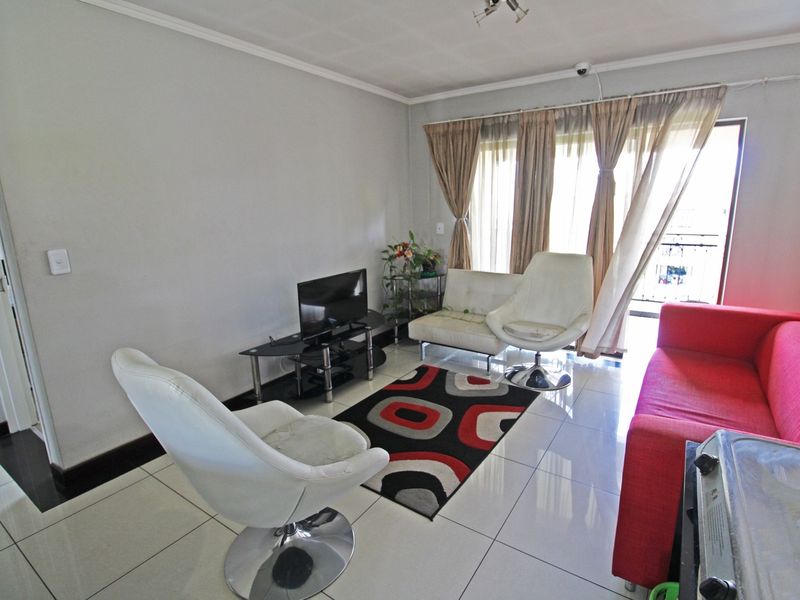 A bright living room featuring large format floor tiles, coving, and a sliding glass door providing access to an outdoor balcony area.