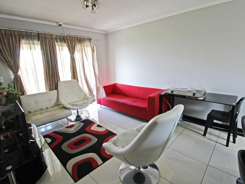A living room area featuring neutral tiled flooring and large windows with curtain tracks, providing a functional and well-lit space.