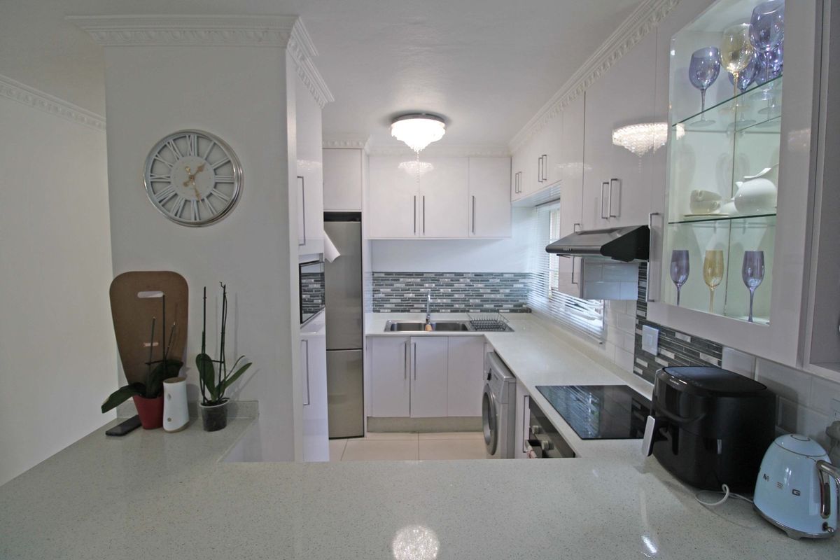 Modern kitchen featuring white high-gloss cabinetry, quartz countertops, mosaic tile backsplash, and integrated appliances, finished with elegant crown molding.