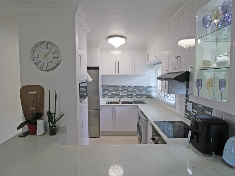 Modern kitchen featuring white high-gloss cabinetry, quartz countertops, mosaic tile backsplash, and integrated appliances, finished with elegant crown molding.