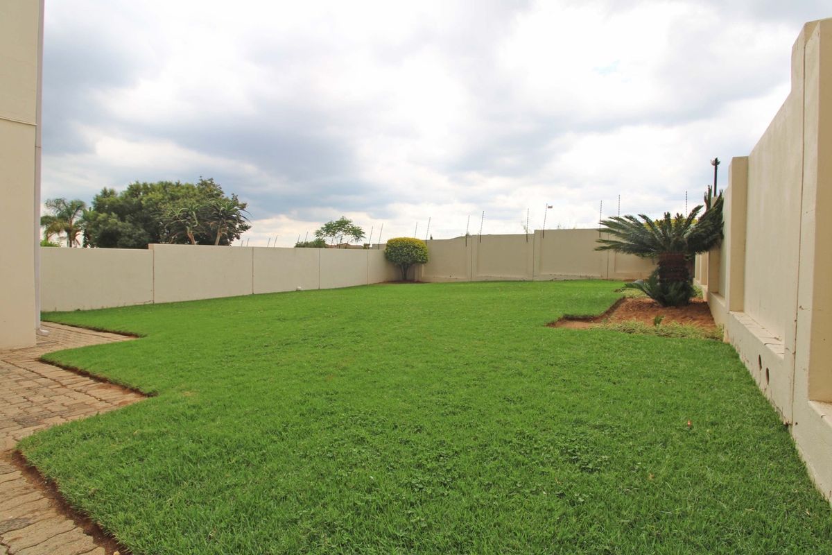A private rear garden featuring a well-maintained lawn, paved walkway, and secure perimeter wall with electric fencing.