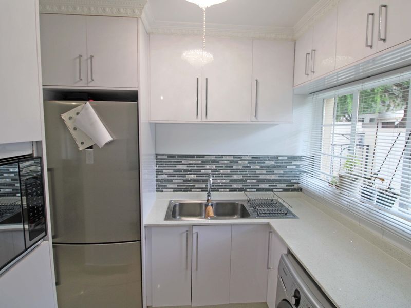 A modern, well-maintained kitchen featuring white high-gloss cabinetry, quartz countertops, a mosaic tile backsplash, and a stainless steel double sink.
