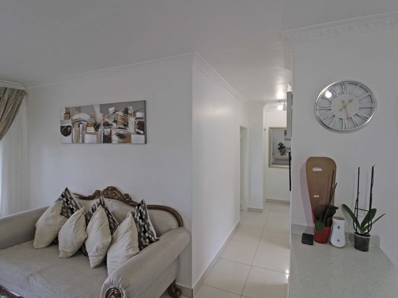 A bright living area featuring elegant crown molding, neutral tiled flooring, and a seamless transition into the hallway.