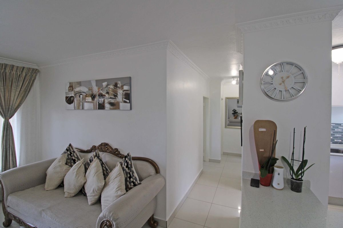 A bright living area featuring elegant crown molding, neutral tiled flooring, and a seamless transition into the hallway.