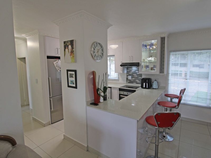 Modern kitchen featuring white cabinetry, quartz countertops, a breakfast bar, and integrated appliances, complemented by tiled flooring and crown molding.