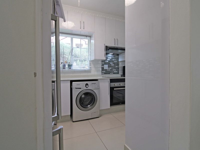 Modern kitchen featuring white cabinetry, tiled backsplash, built-in oven and hob, and tiled flooring, viewed through a doorway.