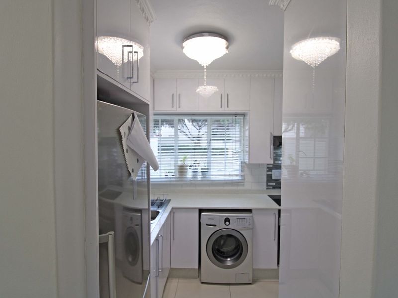 A compact, well-maintained kitchen featuring white cabinetry, tiled backsplash, and integrated laundry facilities, offering a clean and functional workspace.