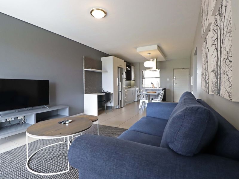 Modern open-plan living area featuring a sleek kitchen with built-in cabinetry, a dedicated workspace, and tiled flooring throughout.